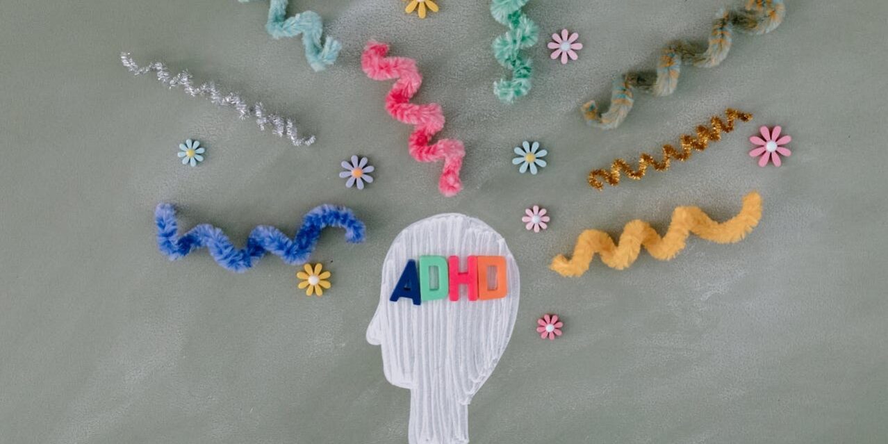 adhd Illustratie van een hoofd met de letters "ADHD" erop, omringd door kleurrijke kronkelige pijpenragers en bloemen, die de chaos en prikkels in het brein symboliseren.