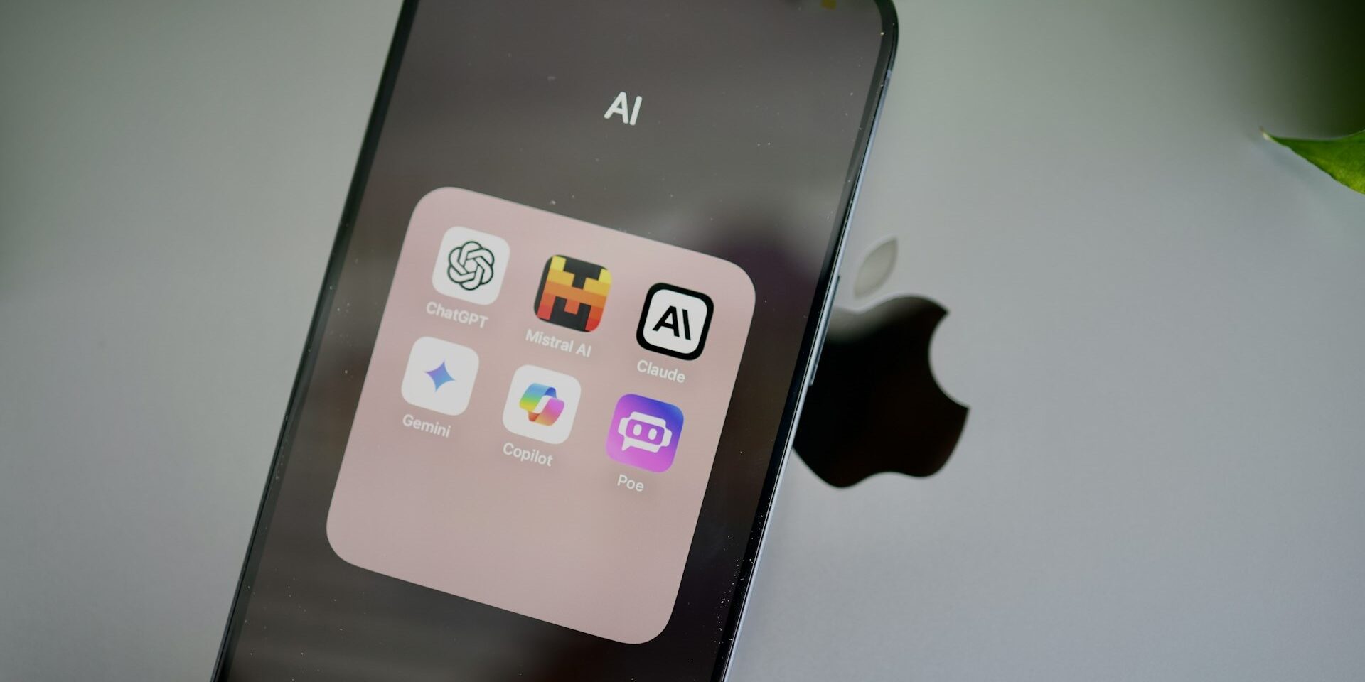 AI-assistenten op smartphone in één overzichtelijke map geplaatst. Smartphone toont map met AI-apps zoals ChatGPT, Copilot, Claude, Gemini, Mistral AI en Poe op het scherm.