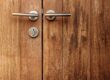 Houten buitendeur met zichtbaar reliëf en metalen handgrepen, toont natuurlijk karakter en onderhoudsbehoefte.
