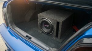 Subwoofer van maatwerk hifi-installatie geplaatst in de kofferbak van een blauwe auto.
