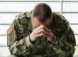 Soldaat in camouflage-uniform met gebogen hoofd en gevouwen handen, zichtbaar worstelend met PTSS