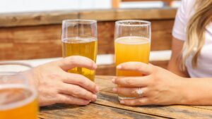 Twee glazen bier, wit en blond, worden vastgehouden tijdens een zonnig moment op het terras.