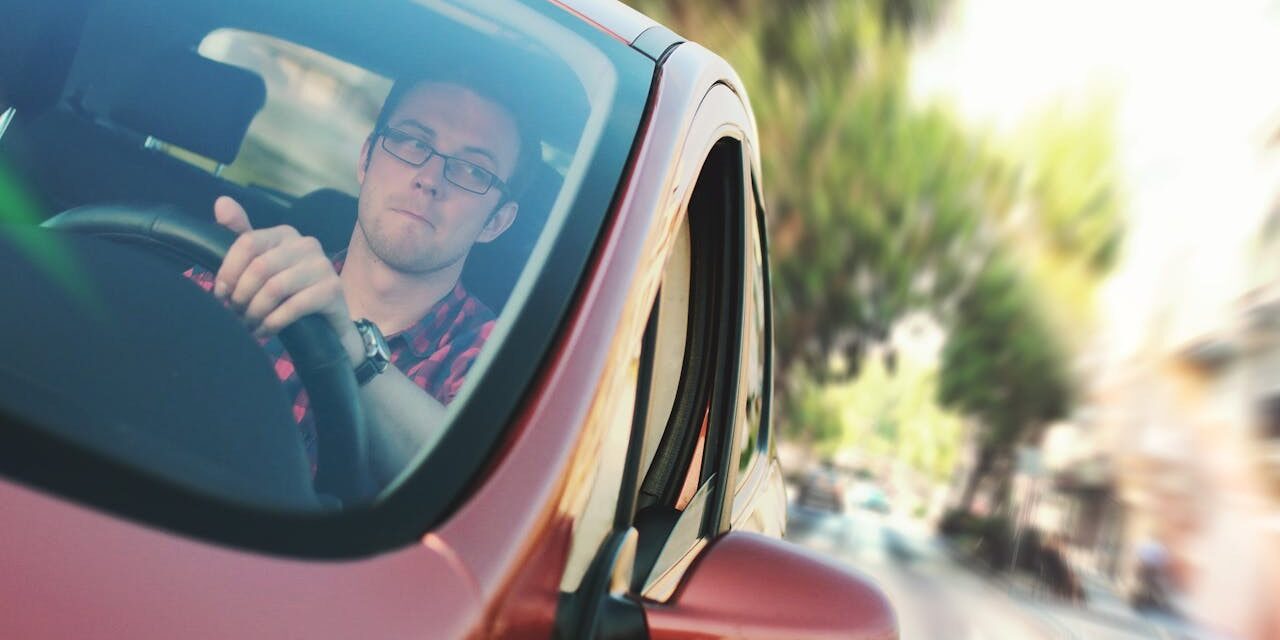 Jonge man met serieuze blik rijdt geconcentreerd in een rode auto tijdens een praktijk- of faalangstexamen