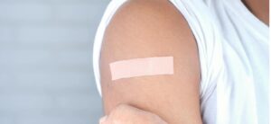 Standaard huidkleurige pleister op bovenarm van een persoon in wit T-shirt na een prik of kleine verwonding