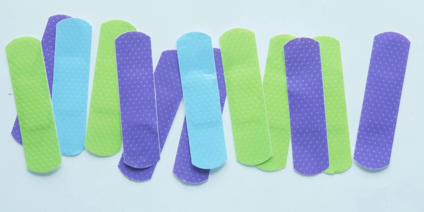 Kleurrijke pleisters in paars, blauw en groen met stippenpatroon, verspreid op een witte ondergrond