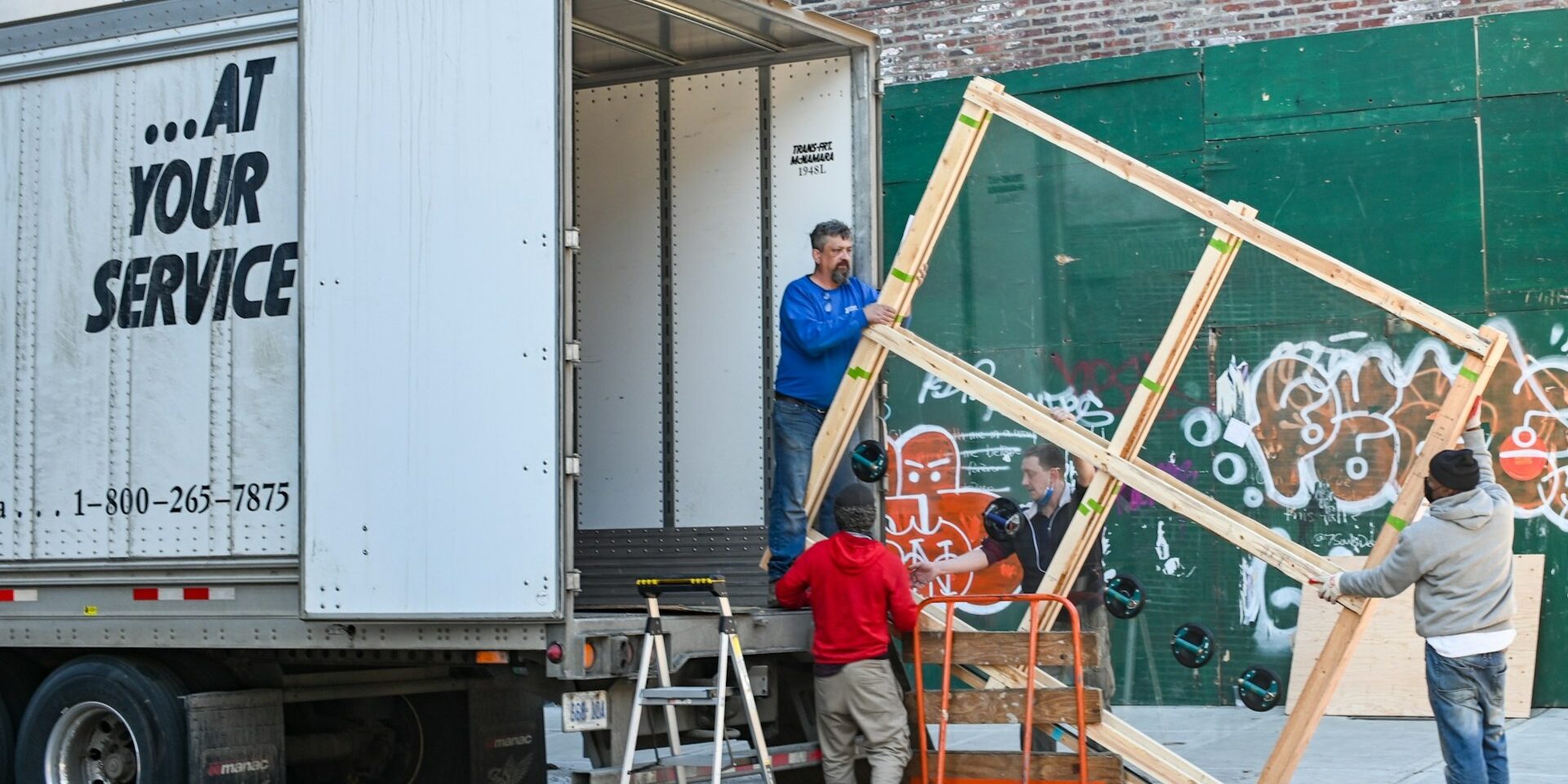 Verhuizers tillen groot raamkozijn uit vrachtwagen tijdens verhuizing zonder verhuislift