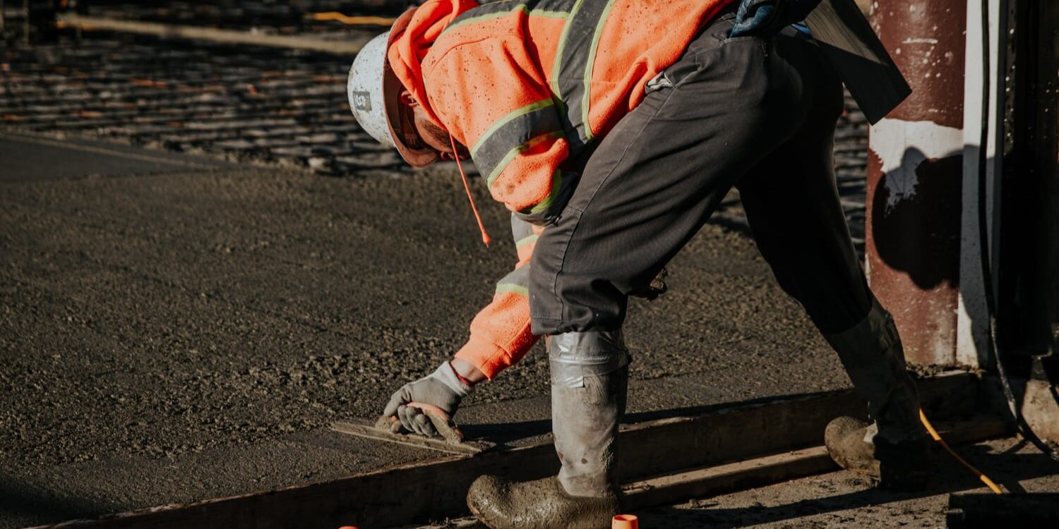Werknemer egaliseert nat beton tijdens aanleg van vloer bij uitleg over betonvloer en cementvloer verschil