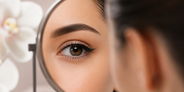 Vrouw bekijkt haar ogen in een spiegel na een infralash- of eyelinerbehandeling