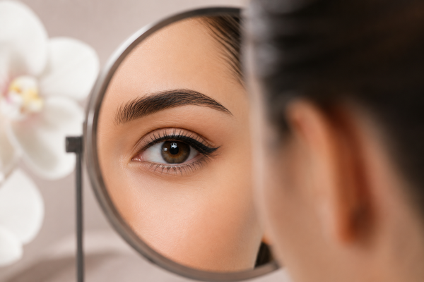Vrouw bekijkt haar ogen in een spiegel na een infralash- of eyelinerbehandeling