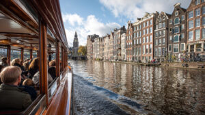 Passagiers genieten van een rondvaart langs historische grachtenpanden en de Klokkentoren op een Amsterdamse gracht