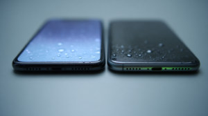 Twee smartphones naast elkaar met waterdruppels op het display, waarbij het rechter toestel een groene gloed bij de laadpoort toont